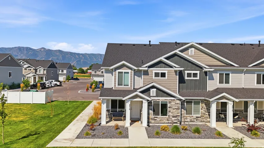 Contemporary townhome featuring a stone and siding facade, covered front porch, dark shingle roof, and an expansive front lawn