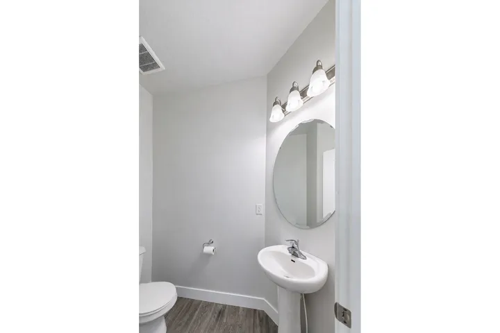 Pedestal sink with chrome faucet and circular mirror with decorative edge