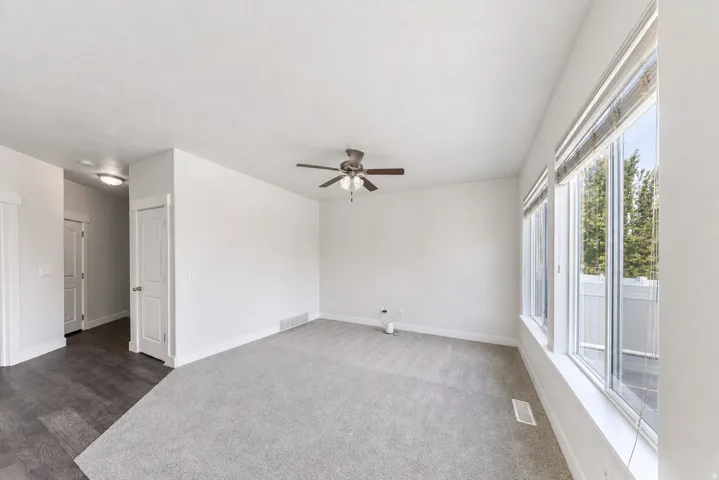 Spacious living area featuring light gray carpeting, a multi-pane window with a white frame, and a dark wood-finish ceiling fan
