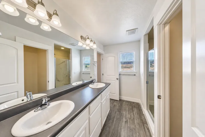 Bathroom featuring a dual vanity with undermount sinks, a large mirror, and wood-finish flooring
