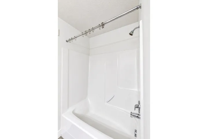 White shower/tub combination with chrome fixtures, a curved shower rod, and a built-in soap dish