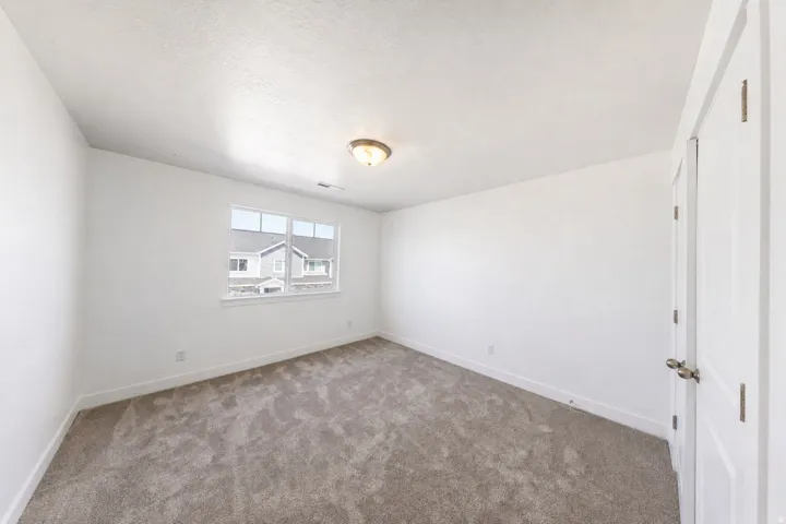 Spacious room featuring gray carpet flooring, clean white walls, and a large window providing natural illumination