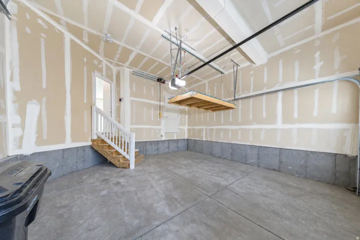 Spacious garage featuring a concrete floor, high vaulted ceiling, interior access door, a built-in staircase with white railing, and an overhead storage rack