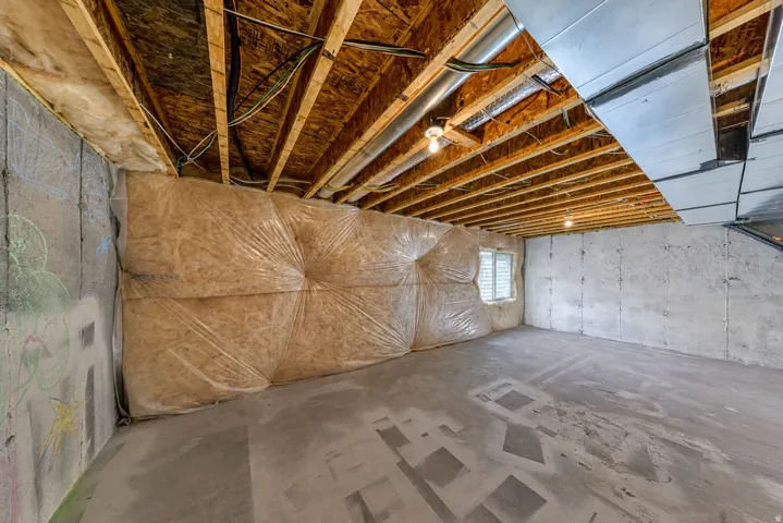 Unfinished basement space featuring exposed wood joists, concrete flooring, and a single window