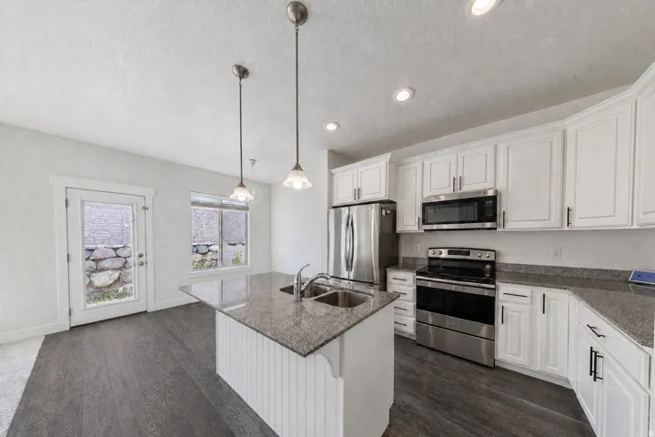 Kitchen featuring white shaker cabinetry, stainless steel appliances, a center island with a double sink, pendant lighting, and wood-finish flooring