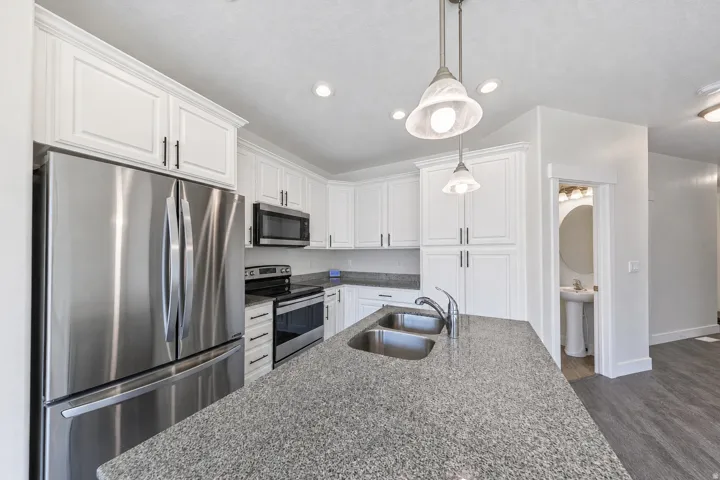 Kitchen featuring white cabinetry, stainless steel appliances, recessed lighting, and a granite-finish island with a double basin sink