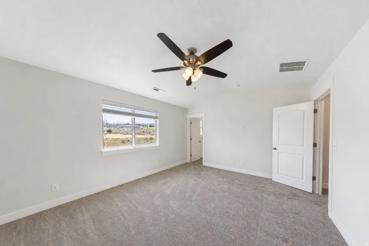 Spacious interior room with light gray carpeting, a vaulted ceiling, and a ceiling fan with integrated lighting