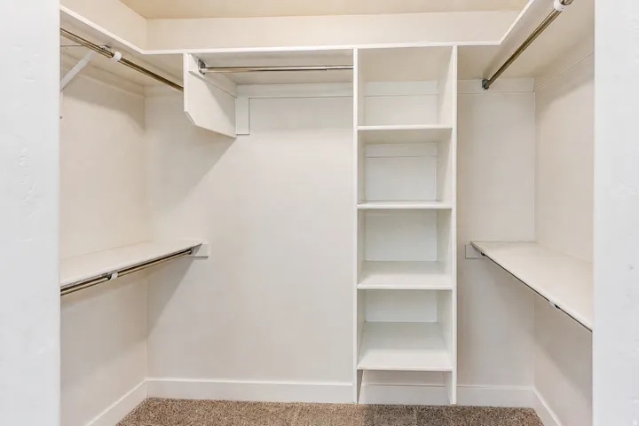 Walk-in closet featuring built-in shelving, multiple hanging rods, and neutral wall tones