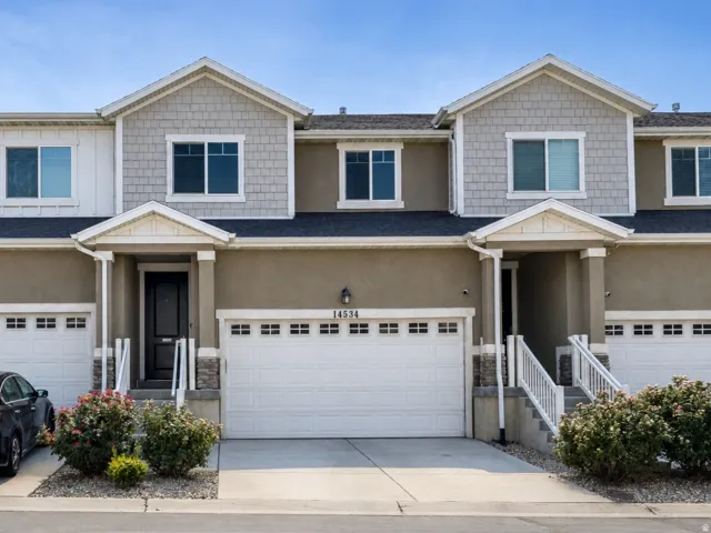 Townhome exterior featuring a neutral stucco and shingle facade, multiple single-car garages with white doors, and a covered entryway with white railings