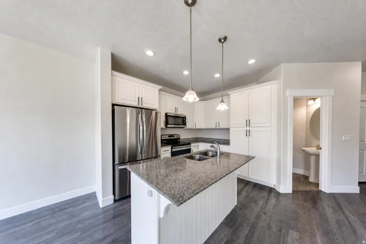 Kitchen featuring a central island with dual sinks, pendant lighting, stainless steel appliances, white cabinetry, and wood-finish flooring