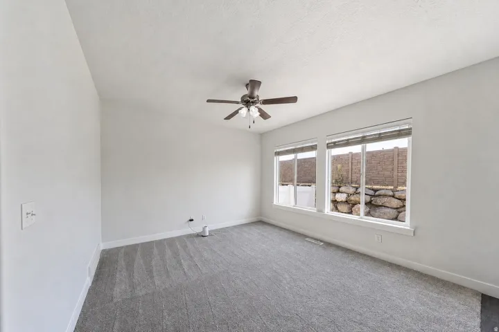 Spacious room with plush gray carpeting, crisp white walls, and a ceiling fan
