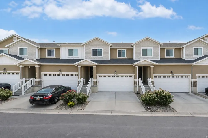 Exterior featuring a tan stucco finish, white trim details, two-car garages, a dark shingle roof, and distinct entryways with stairs
