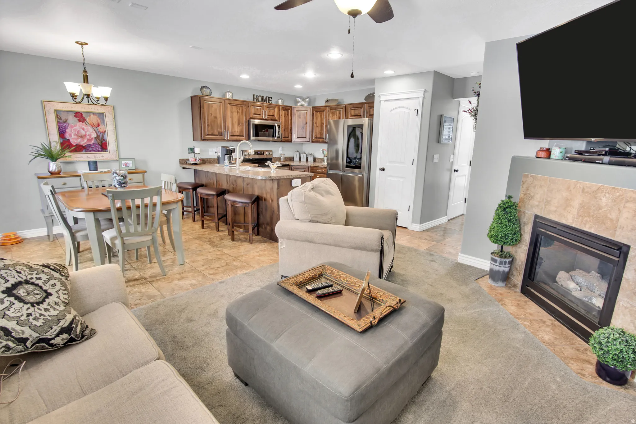 Inviting living space featuring a corner fireplace with tile surround, wood-finish cabinetry, stainless steel appliances, and a kitchen island with seating