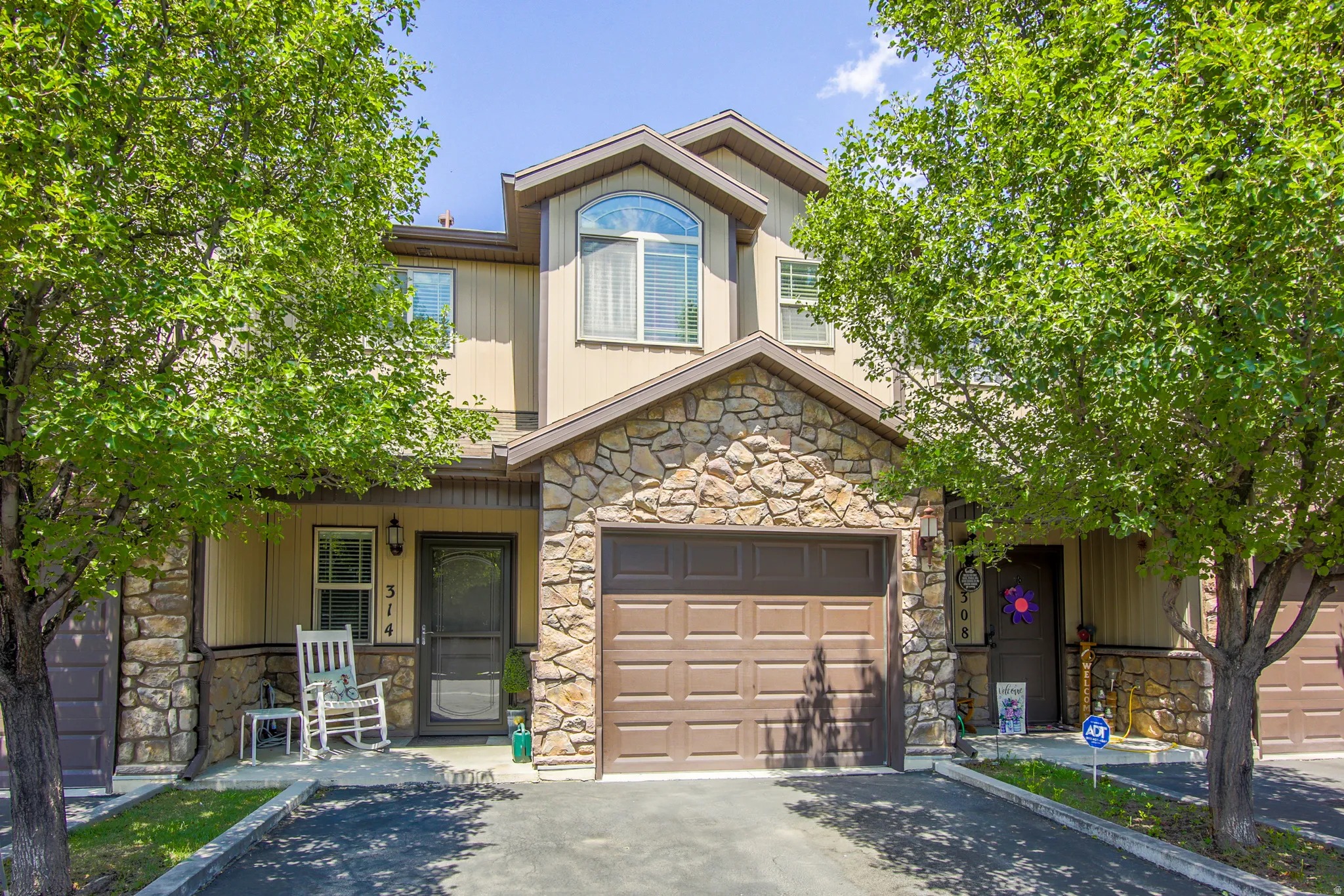 Townhome exterior featuring a stone and stucco facade, a single-car garage, an arched window, and a paved driveway