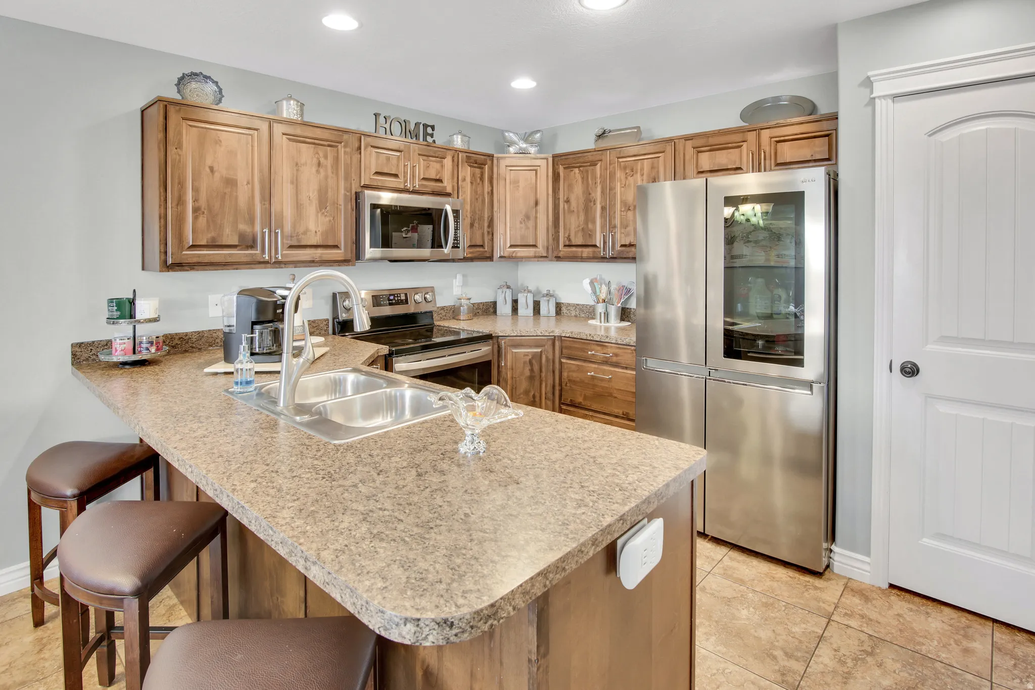 Kitchen featuring wood-finish cabinetry, speckled countertops, stainless steel appliances, and a double basin sink with a high-arc faucet