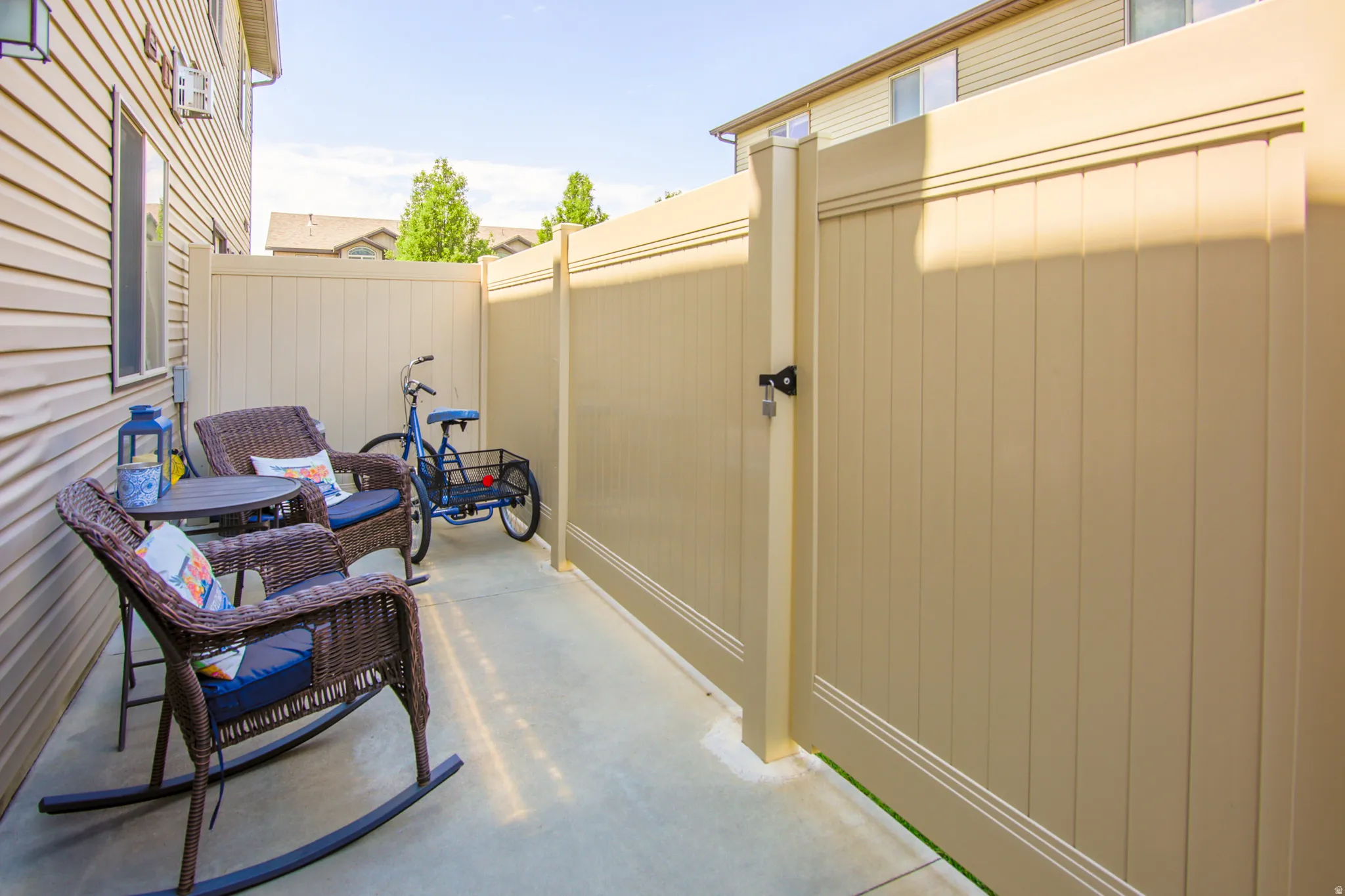 Paved concrete patio featuring a tan vinyl privacy fence with an integrated gate