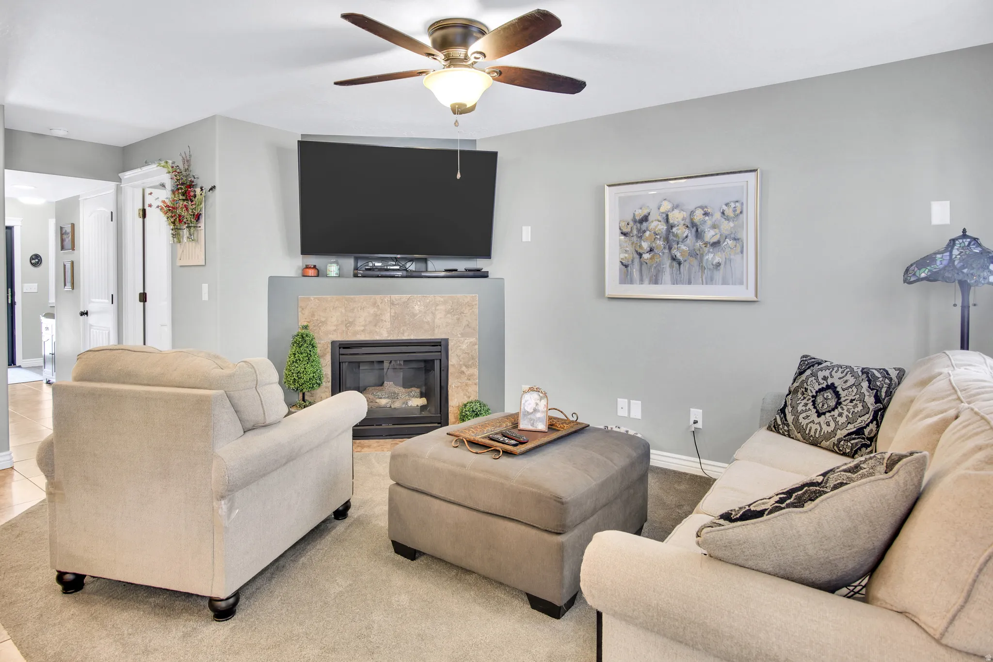 Living area featuring a gas fireplace with a tiled surround, a ceiling fan, and light gray wall paint