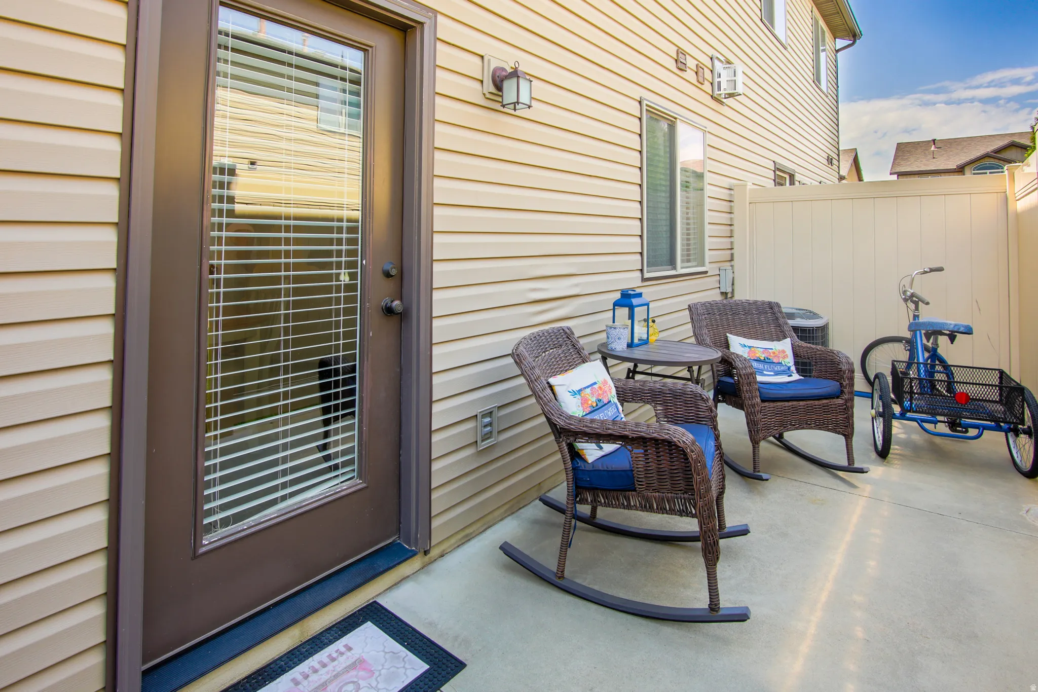 Private concrete patio area featuring light-toned vinyl siding, a full-lite exterior door with integrated blinds, and an exterior wall light fixture