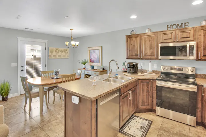 Kitchen featuring L-shaped countertop with dual basin stainless steel sink, stainless steel appliances, wood-finish cabinetry, and tiled flooring