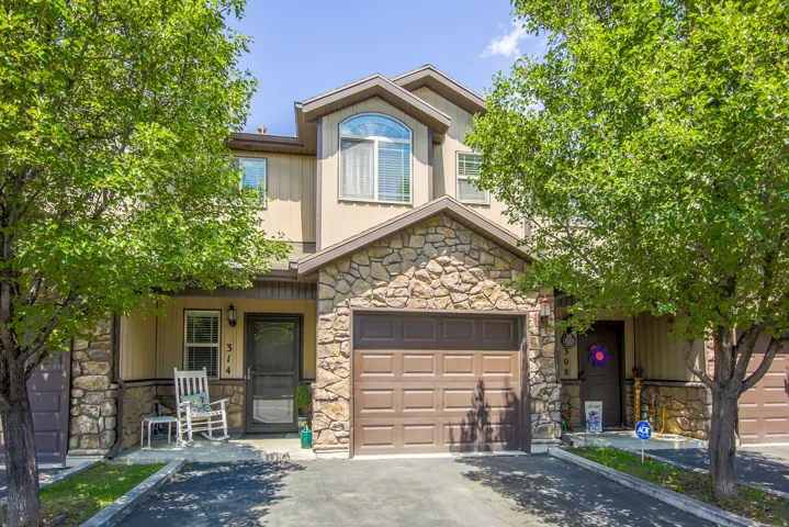 Townhome exterior featuring a stone and stucco facade, a single-car garage, an arched window, and a paved driveway