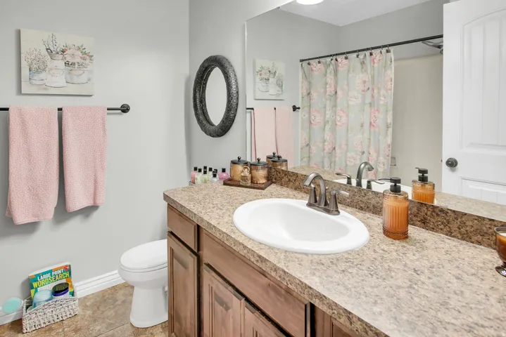 Bathroom featuring a single vanity with wood-finish cabinetry, a speckled countertop, and an integrated sink with a bronze-tone faucet