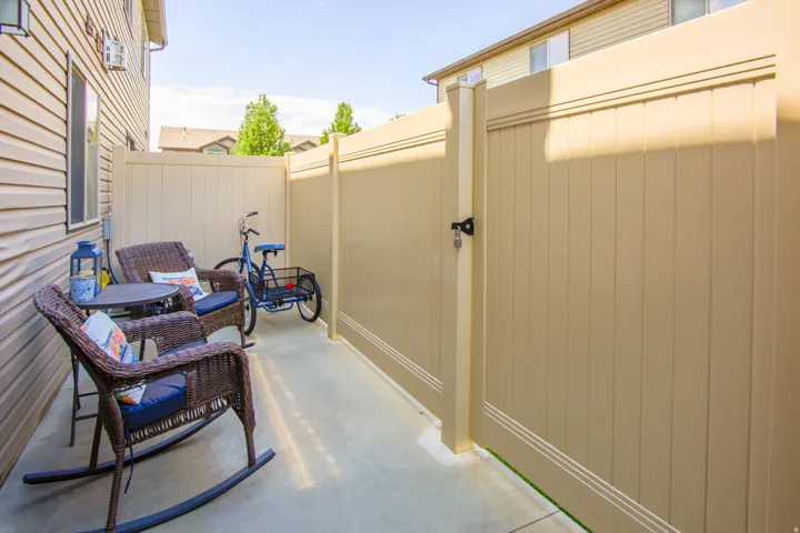 Paved concrete patio featuring a tan vinyl privacy fence with an integrated gate