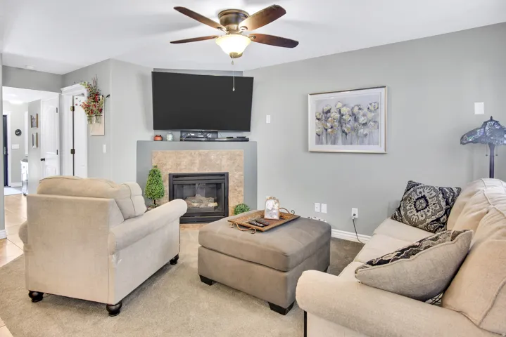 Living area featuring a gas fireplace with a tiled surround, a ceiling fan, and light gray wall paint