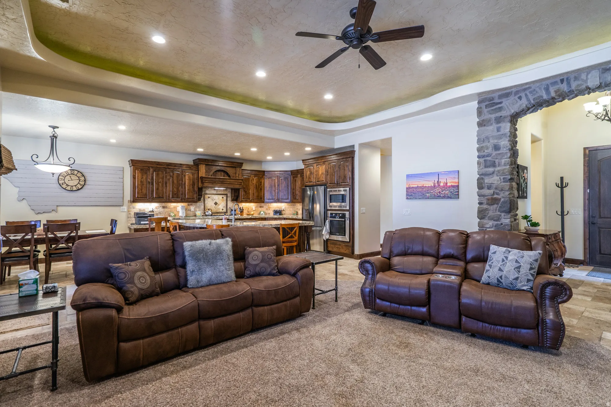 Open-concept living area with tray ceiling, recessed lighting, ceiling fan, stone archway, and wood-finish cabinetry