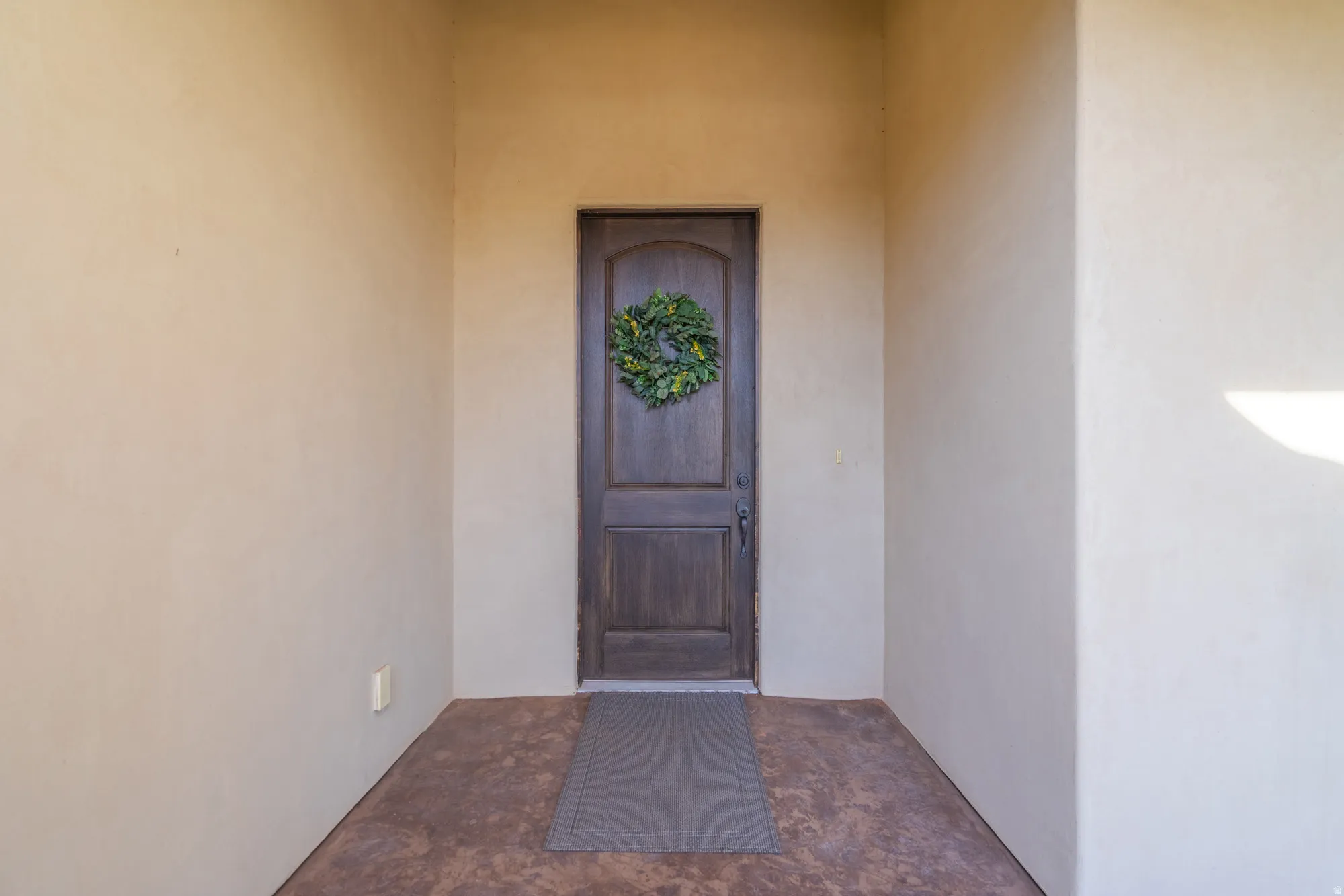 Recessed entry featuring a dark wood-finish door with curved top panel, stucco walls, and a textured concrete floor