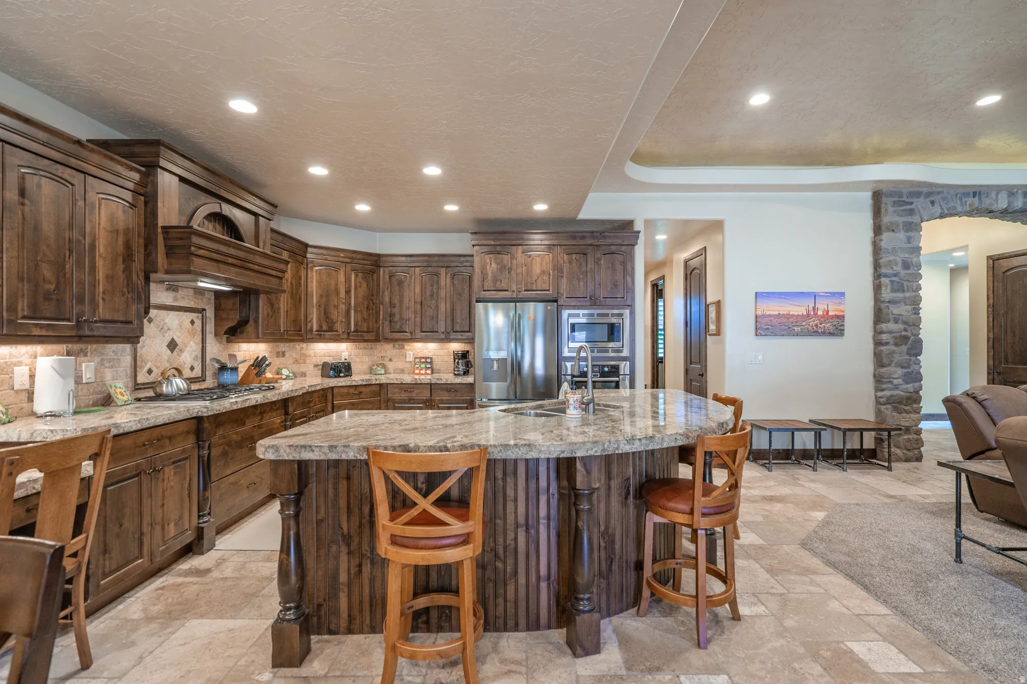 Gourmet kitchen featuring rich wood cabinetry, stainless steel appliances, and a expansive marble-topped island with seating for multiple guests