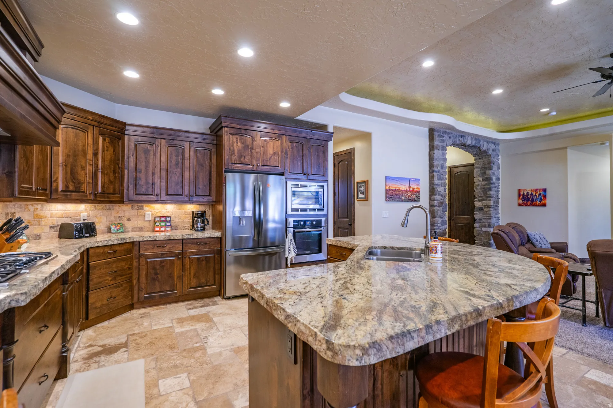 Gourmet kitchen with rich wood cabinetry, stainless steel appliances, stone tile flooring, a large island featuring an undermount sink, and recessed lighting