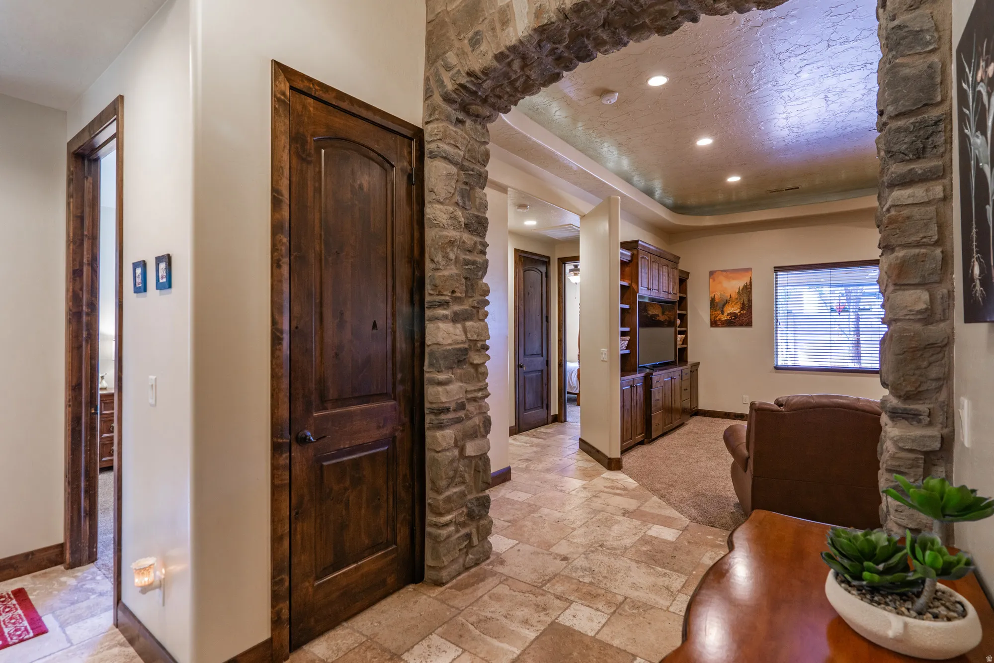 Stone archway entrance to a space featuring recessed lighting and a built-in wood media cabinet