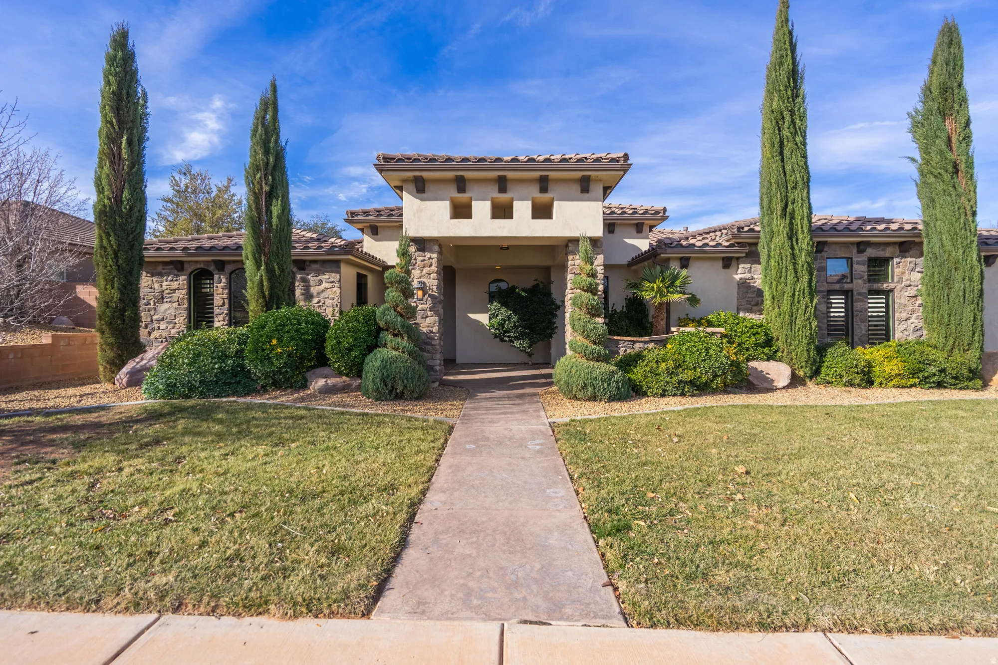 Stucco and stone facade with a tiled roof, featuring a covered entryway, decorative landscaping, and a concrete pathway