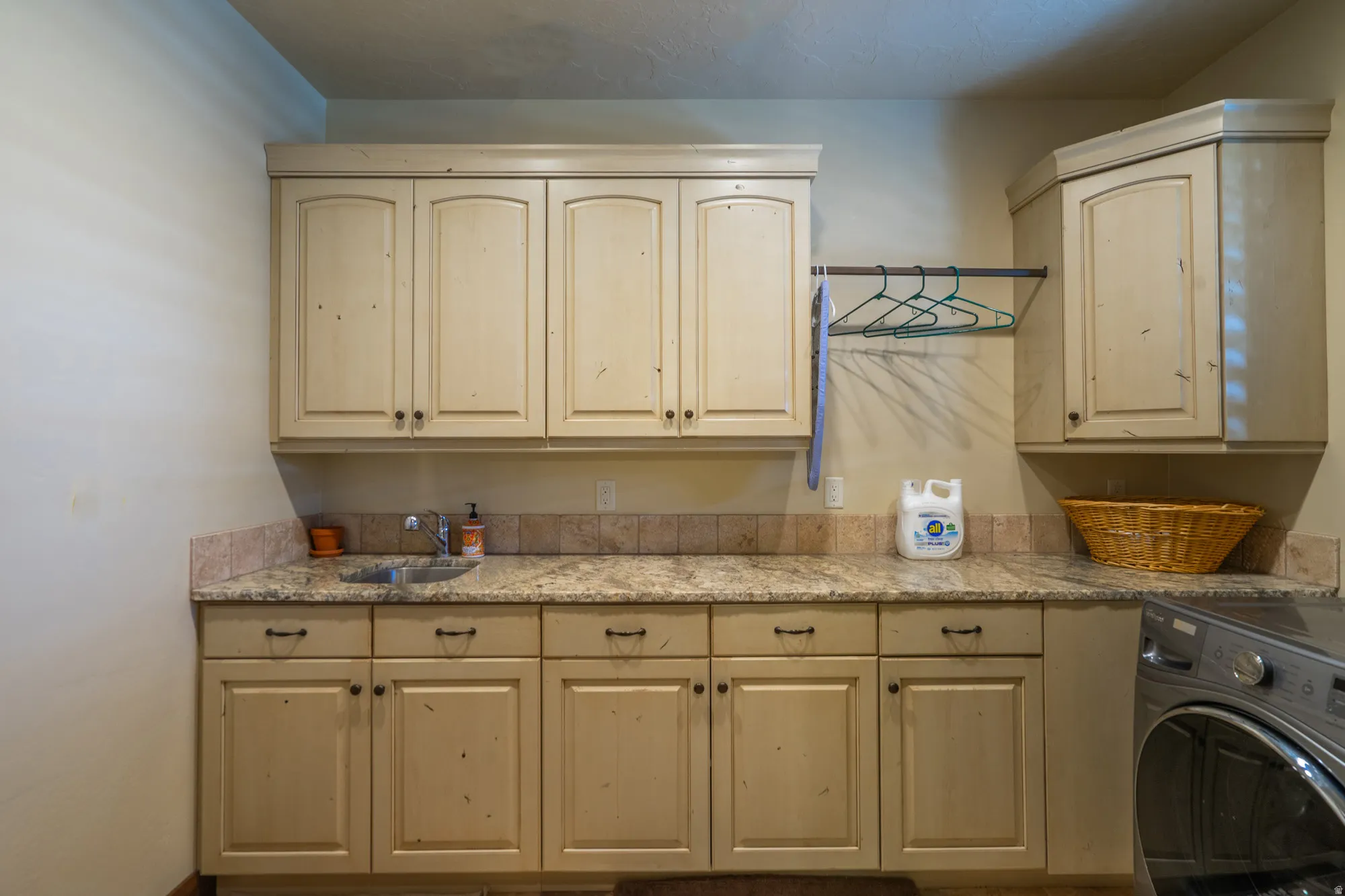 Laundry room featuring extensive cabinetry, a built-in sink, stone countertops, and a tile backsplash