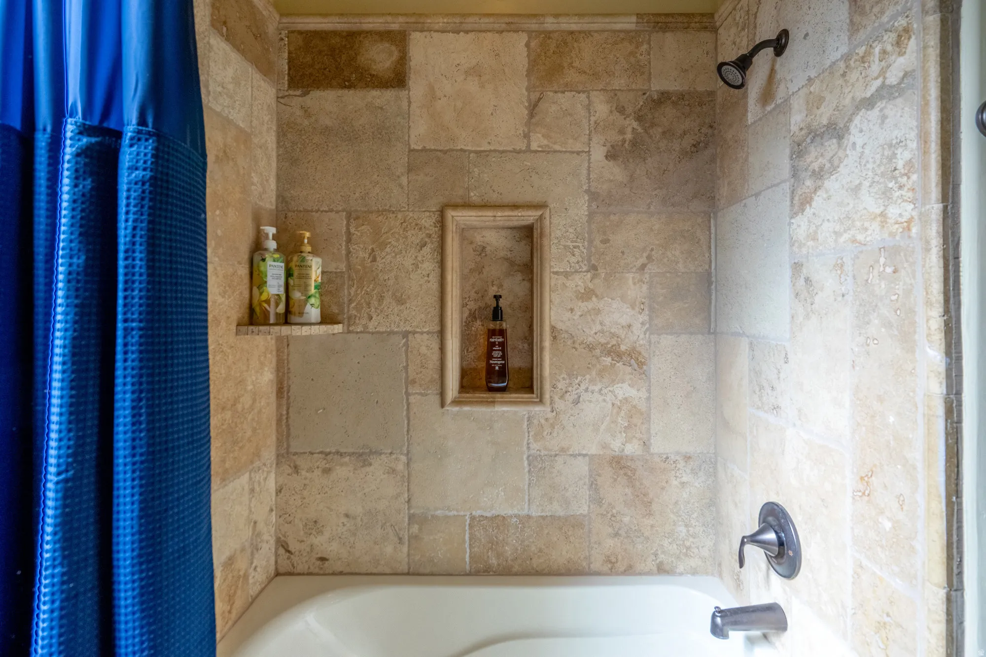 Bathtub with full-height tile surround, featuring an integrated shower niche and a corner shelf