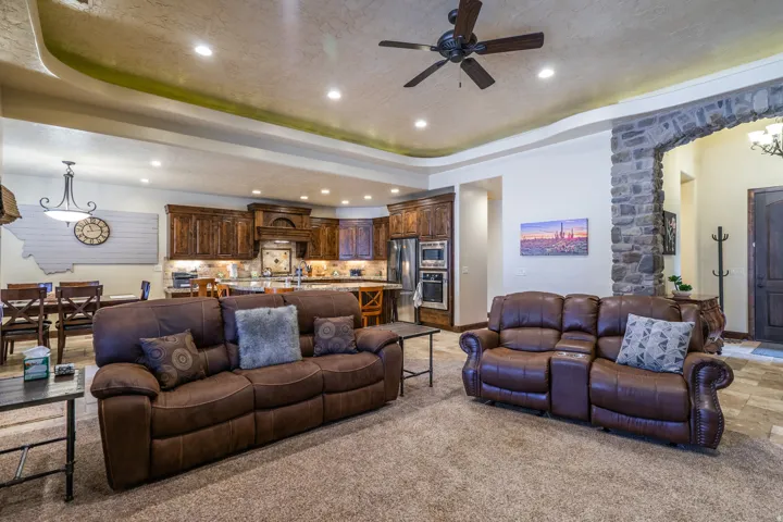 Open-concept living area with tray ceiling, recessed lighting, ceiling fan, stone archway, and wood-finish cabinetry