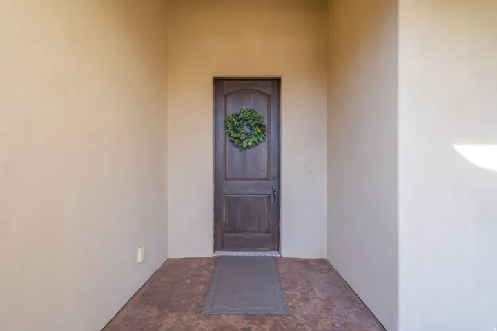 Recessed entry featuring a dark wood-finish door with curved top panel, stucco walls, and a textured concrete floor