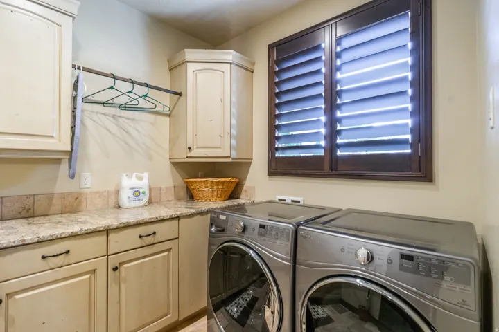 Functional utility space featuring light-colored cabinetry, a speckled countertop, and a tiled backsplash