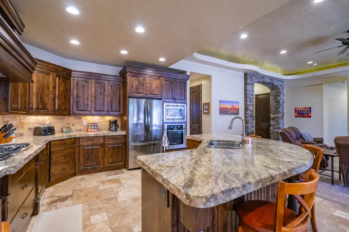 Gourmet kitchen with rich wood cabinetry, stainless steel appliances, stone tile flooring, a large island featuring an undermount sink, and recessed lighting