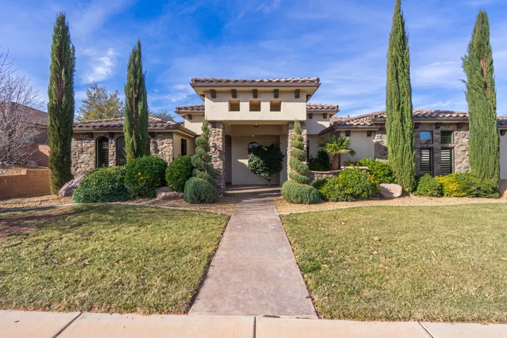 Stucco and stone facade with a tiled roof, featuring a covered entryway, decorative landscaping, and a concrete pathway