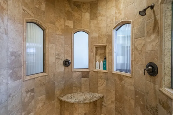 Stone-tiled shower featuring an integrated bench seat, a recessed shower niche, and a bronze showerhead with coordinating fixtures