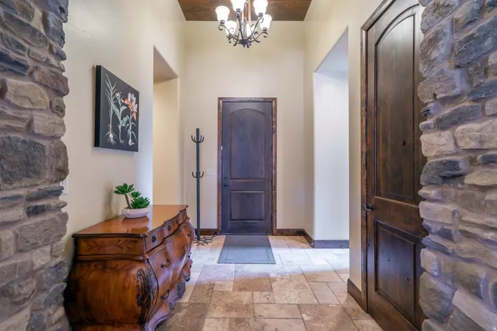 Entryway featuring natural stone wall accents, wood-finish arch-top doors, tile flooring, and a coffered wood-finish ceiling with an attached chandelier