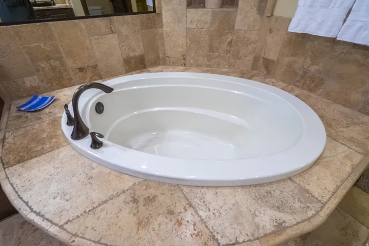 Built-in soaking tub featuring an oil-rubbed bronze faucet, surrounded by natural stone tile, and a decorative tile backsplash