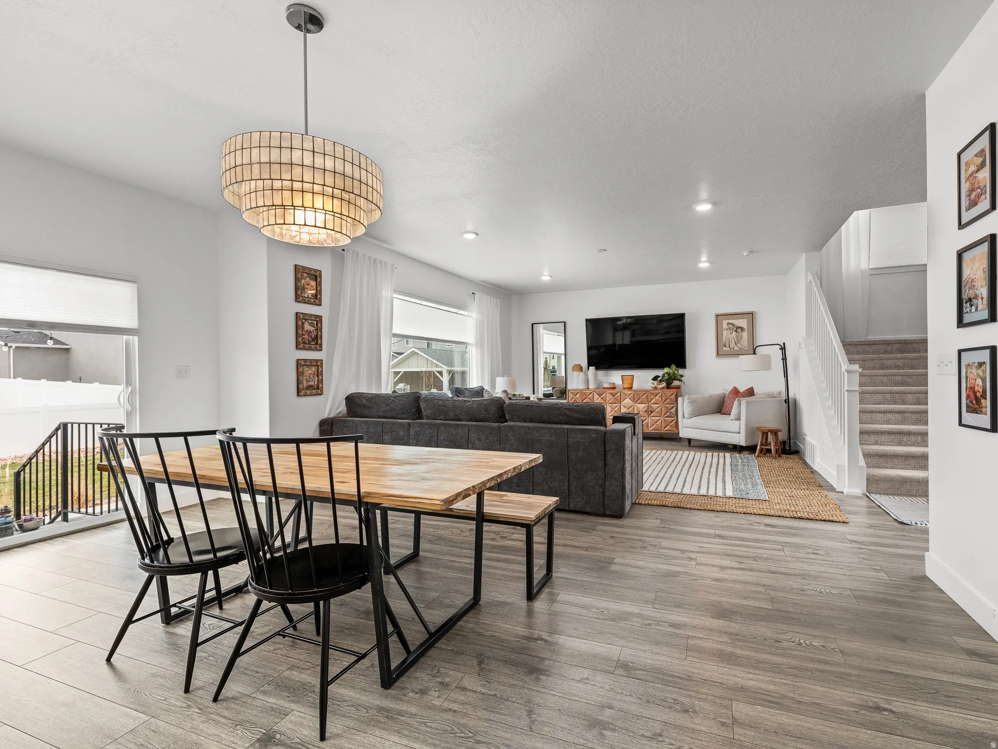 Open-concept dining and living area featuring wood-finish flooring, a tiered pendant light fixture, recessed lighting, and a carpeted staircase with white railings