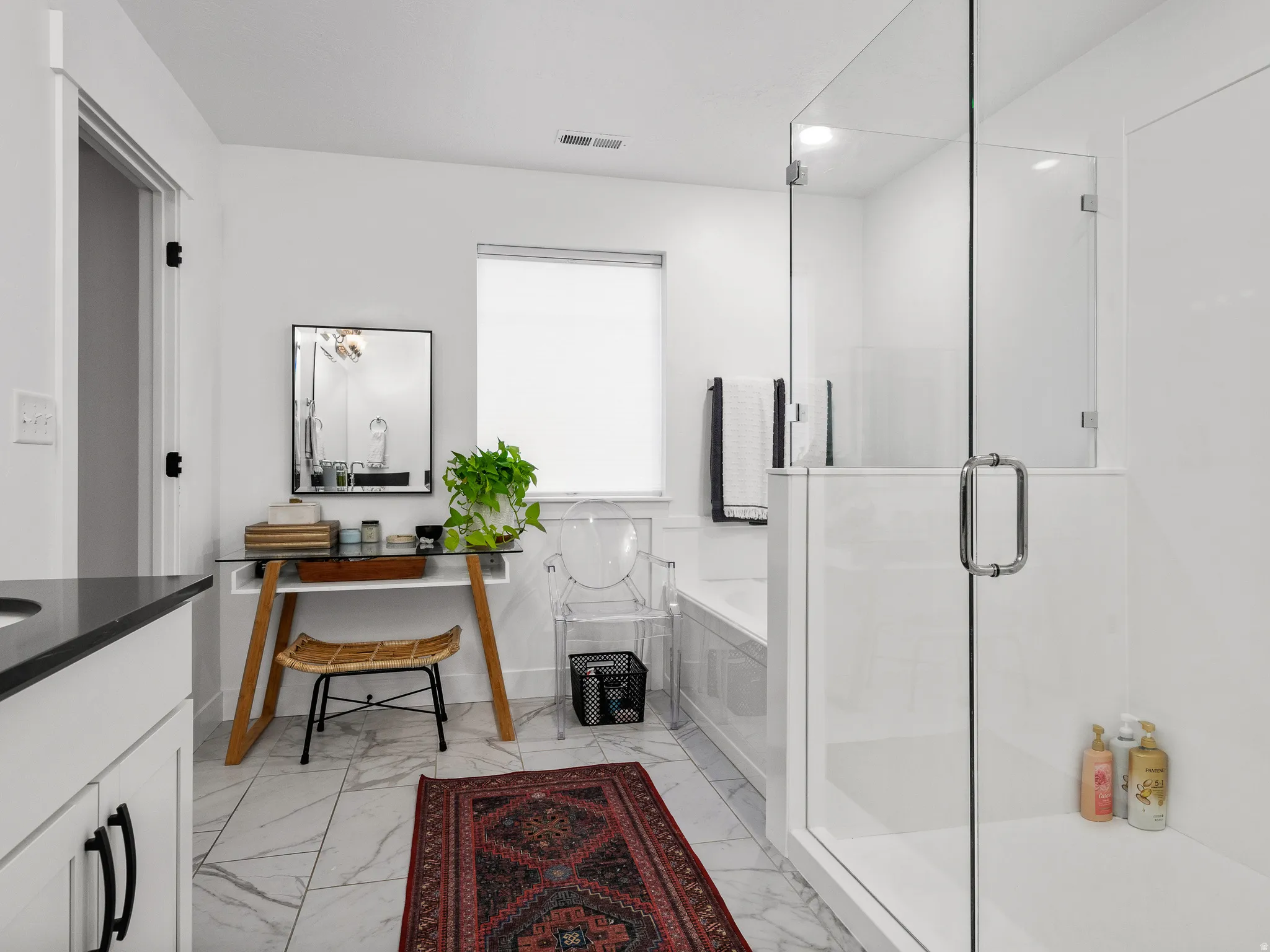 Modern bathroom featuring a frameless glass shower enclosure, a built-in soaking tub, a single vanity with dark countertop, and marble-look tile flooring