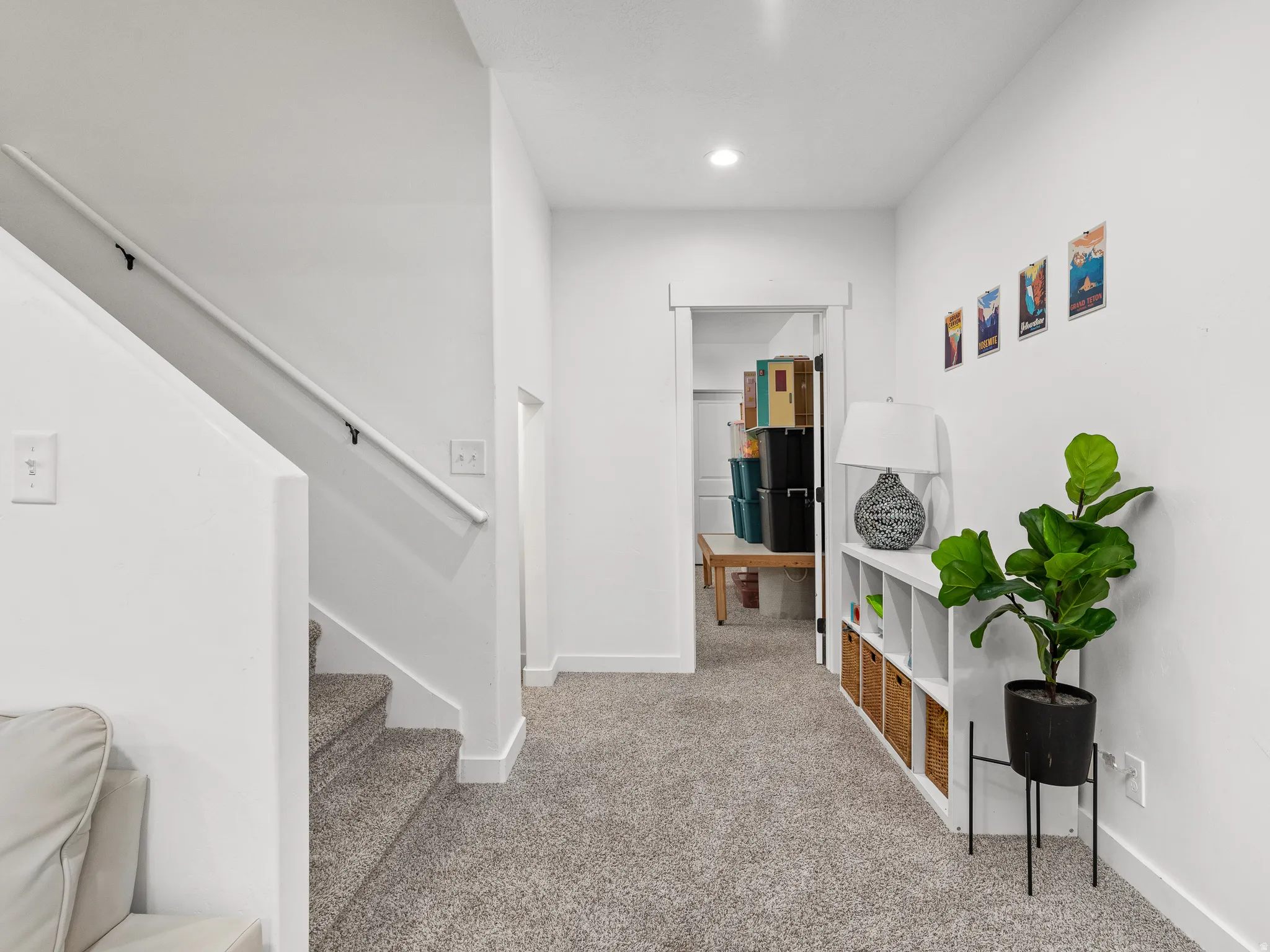 Carpeted hallway featuring a staircase with a white handrail, recessed lighting, and a doorway opening to an interior room
