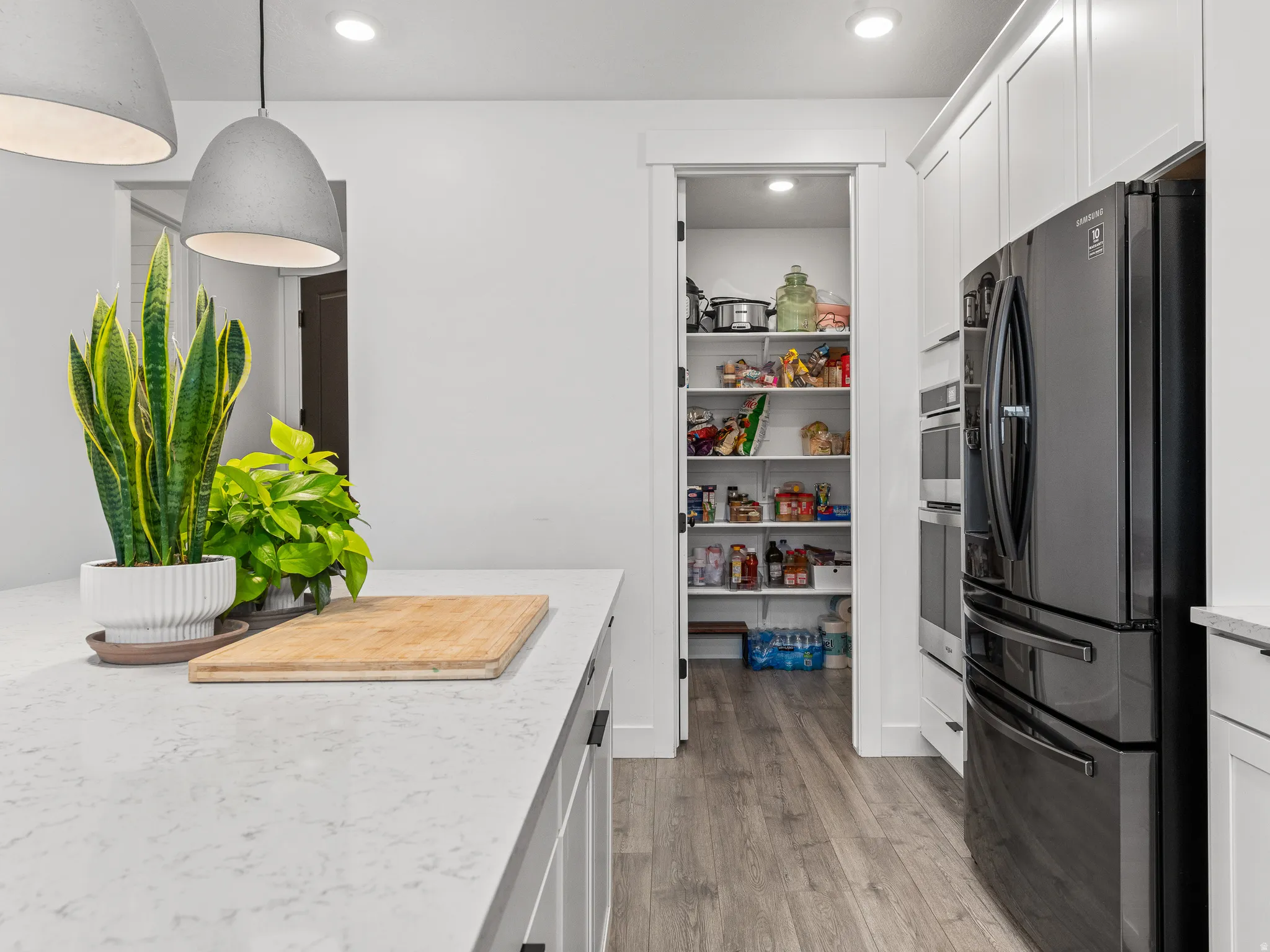 Kitchen island featuring a light-toned countertop, white cabinetry with dark hardware, and two pendant lights