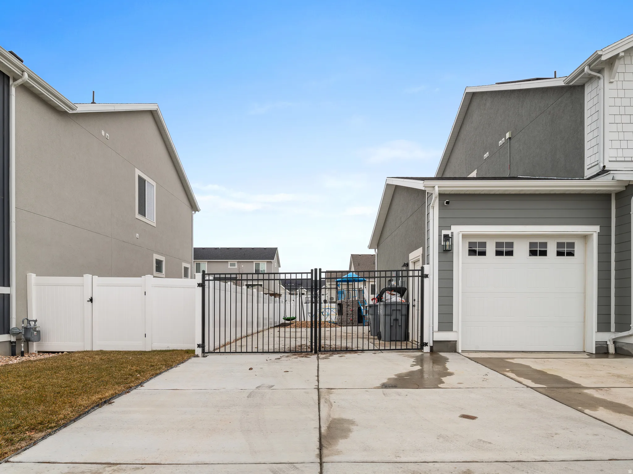 Concrete driveway featuring a black metal gate and an attached garage with a paneled door