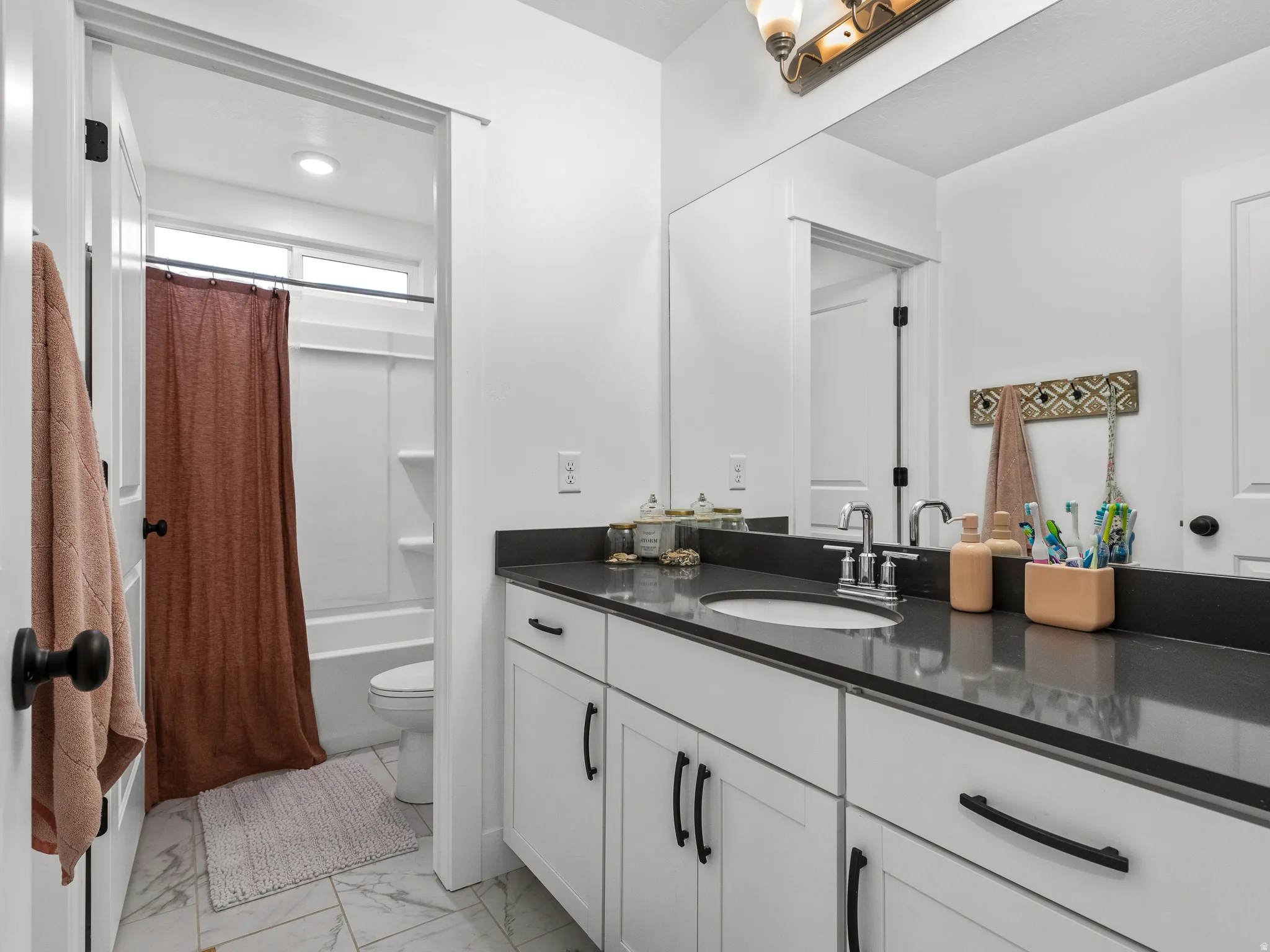 Bathroom featuring a white vanity with dark countertops and hardware, a built-in sink, and a large wall-mounted mirror