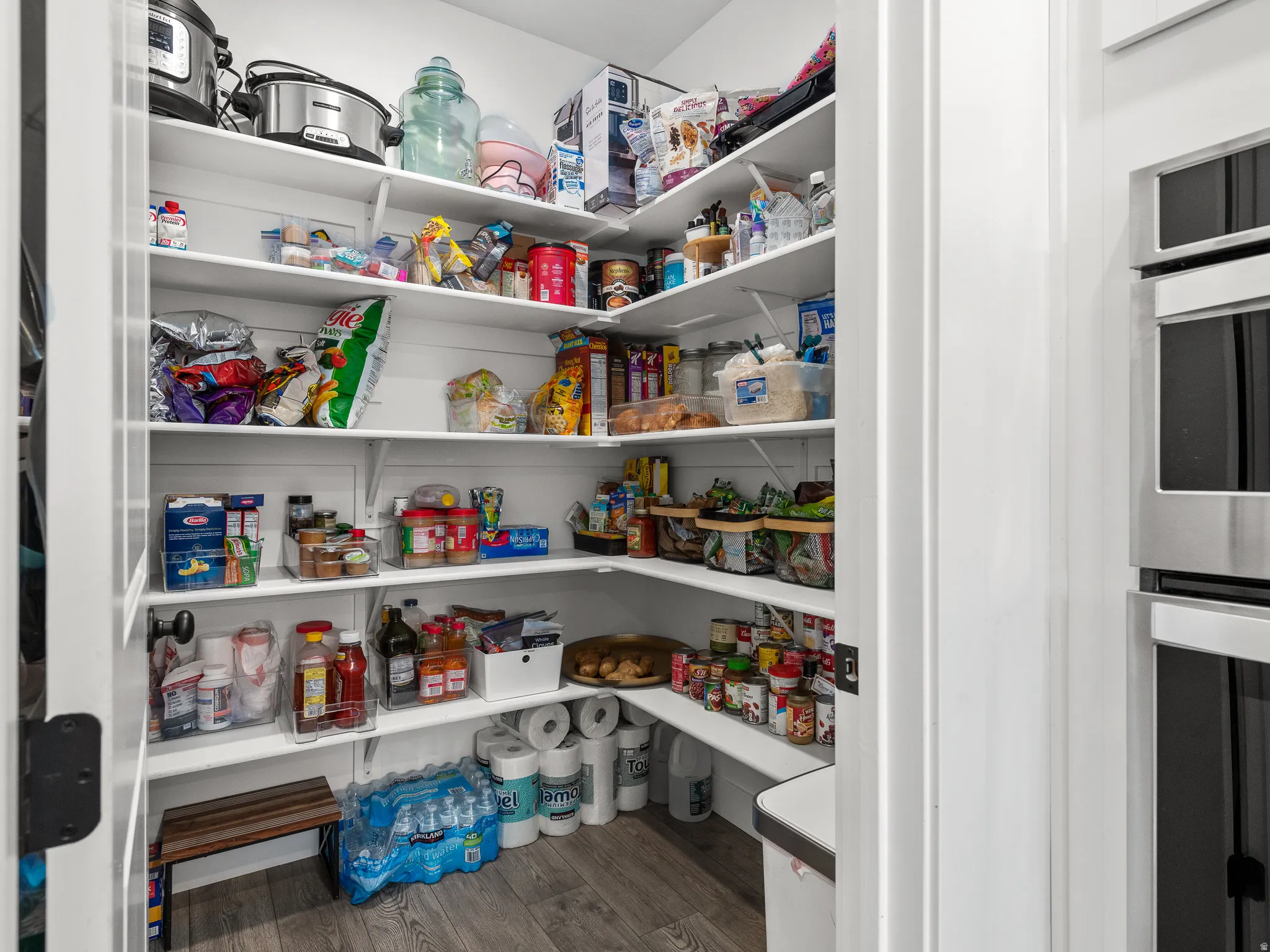 Walk-in pantry featuring white shelving, wood-finish flooring, and ample storage capacity